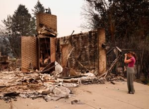 A woman stands in front of her grandparents' home, where she previously lived, after it was destroyed by a wildfire in Spokane, Washington, Aug. 2, 2026. Photo: Reuters